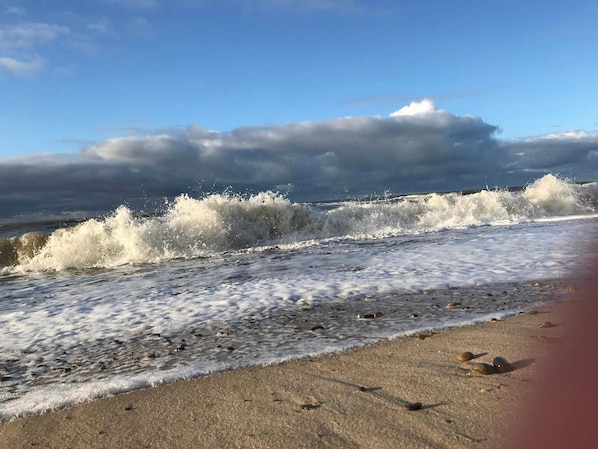 Une plage oĂč les vagues se brisent sur le rivage, un ciel dĂ©gagĂ© et un sentier longeant la plage.