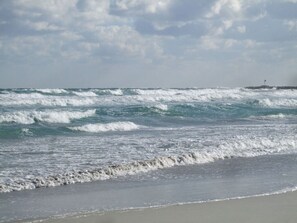 A beach with waves and a lighthouse in the distance.