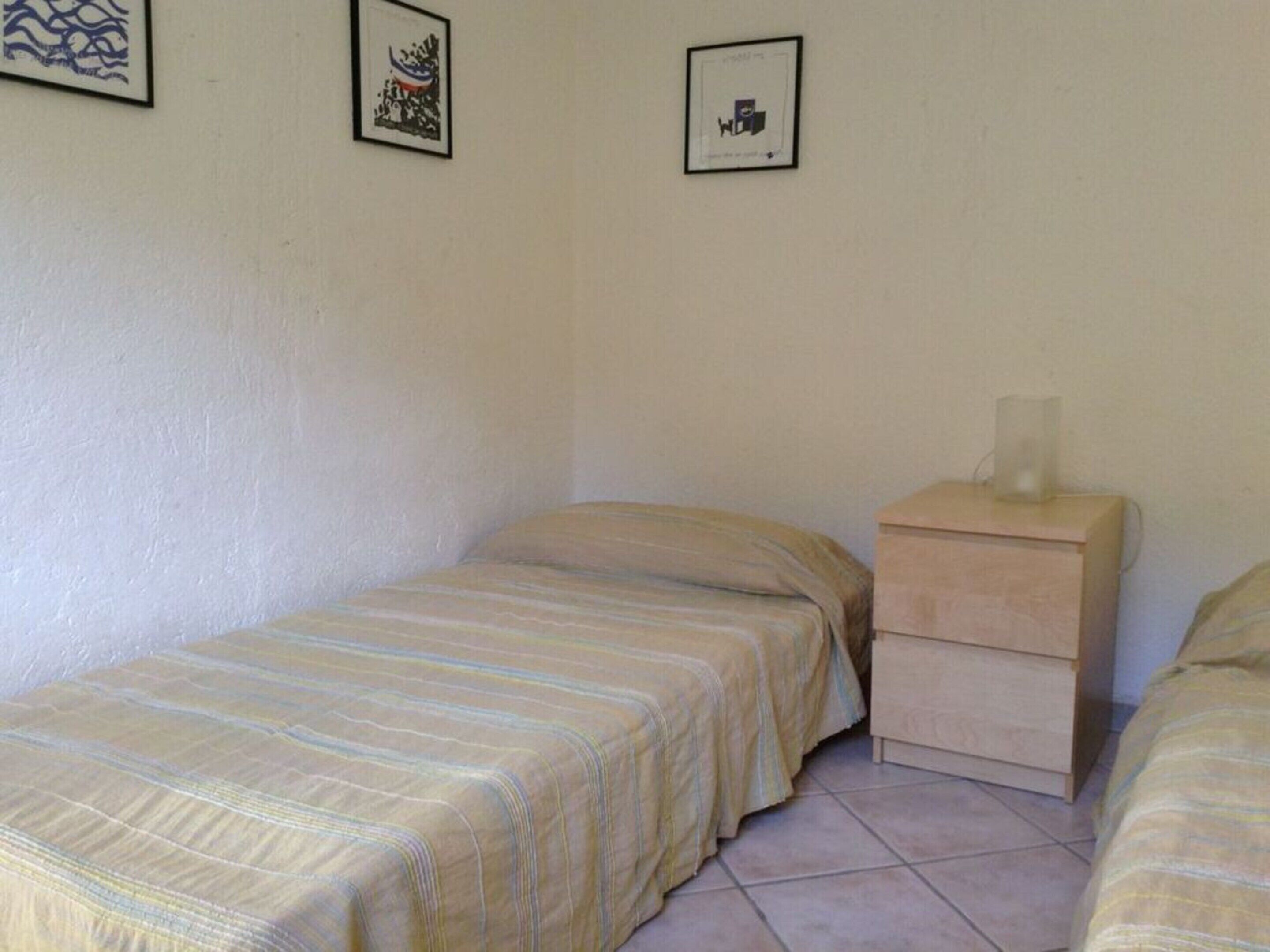 Een kleine, éénkameraccommodatie met een bed, nachtkastje en een lijst met een afbeelding aan de muur.