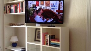 A television mounted on a wall above a bookshelf with books and a lamp. - Casa Felicita Comfortable Holiday Residence (San Teodoro)