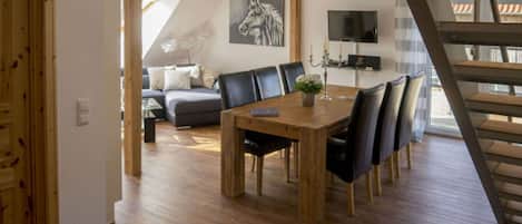 A modern living room with a wooden dining table, black chairs, a grey sofa, and a mounted TV.