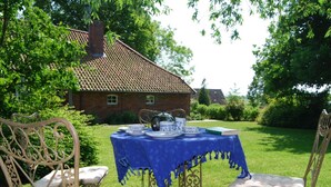 An outdoor dining area with a table set for tea, surrounded by ornate chairs, in a garden with a brick building in the background. - - Exclusively Restored Gulfhof (Wangerland)