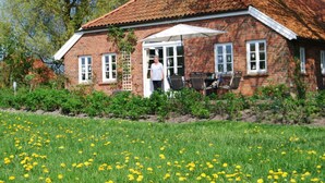 A brick house with a red-tiled roof, a white door, and a patio with outdoor furniture. - - Exclusively Restored Gulfhof (Wangerland)