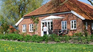 A brick house with a red-tiled roof, a white door, and a patio with outdoor furniture.