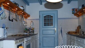 A kitchen with white cabinets, a blue door, and various kitchen utensils hanging on the wall. - - Exclusively Restored Gulfhof (Wangerland)