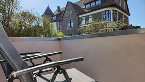 A balcony with a chair and a view of a large house with multiple windows and a chimney. - Sound of the sea Modern Retreat (Wangerooge)