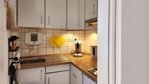 A kitchen with white cabinets, a wooden countertop, a sink, a kettle, and yellow oven mitts hanging on the wall. - Sound of the sea Modern Retreat (Wangerooge)