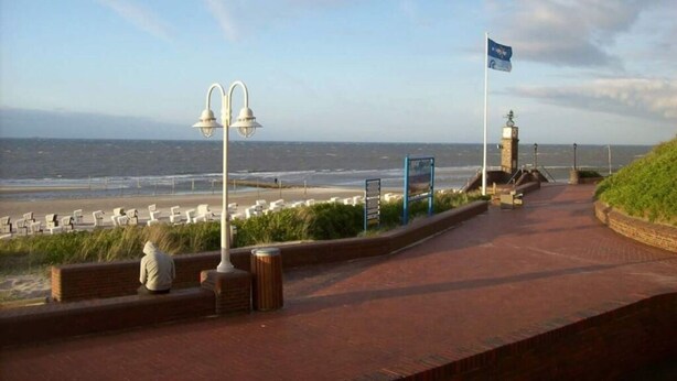 A coastal walkway with a view of the sea, a flag, and a lamp post. - Sound of the sea Modern Retreat (Wangerooge)