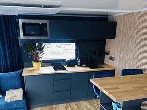 A compact kitchen with a microwave, stove, and sink. There's a window with a view, a plant on the counter, and a blue chair. - Premium Houseboat Blue Lagoon (Lübeck)