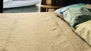 Een bed met uitzicht op een zeilboot op het water door een raam.