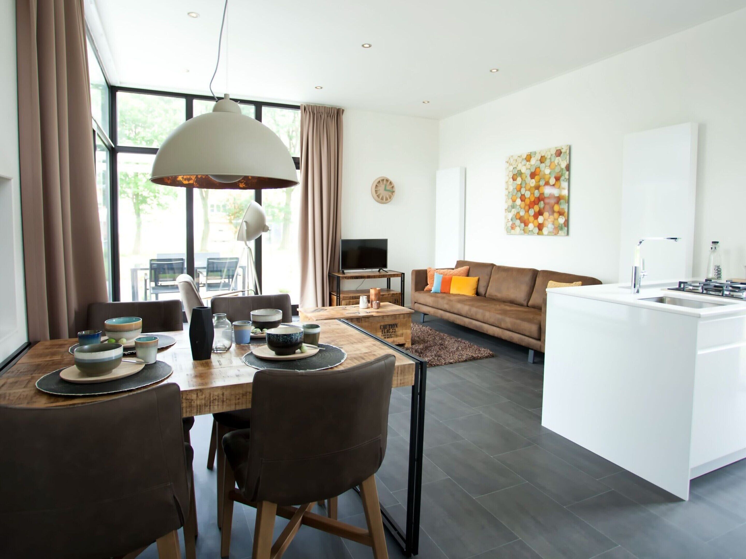 Un espacio de estar moderno con comedor, sofá, televisión y isla de cocina.
