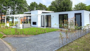 Une maison moderne à deux étages, dotée d’un espace extérieur aménagé et couvert, ainsi que d’une allée en gravier.