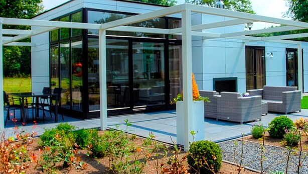Une maison moderne en verre dotée d’un patio, d’un espace salon extérieur et d’un jardin.