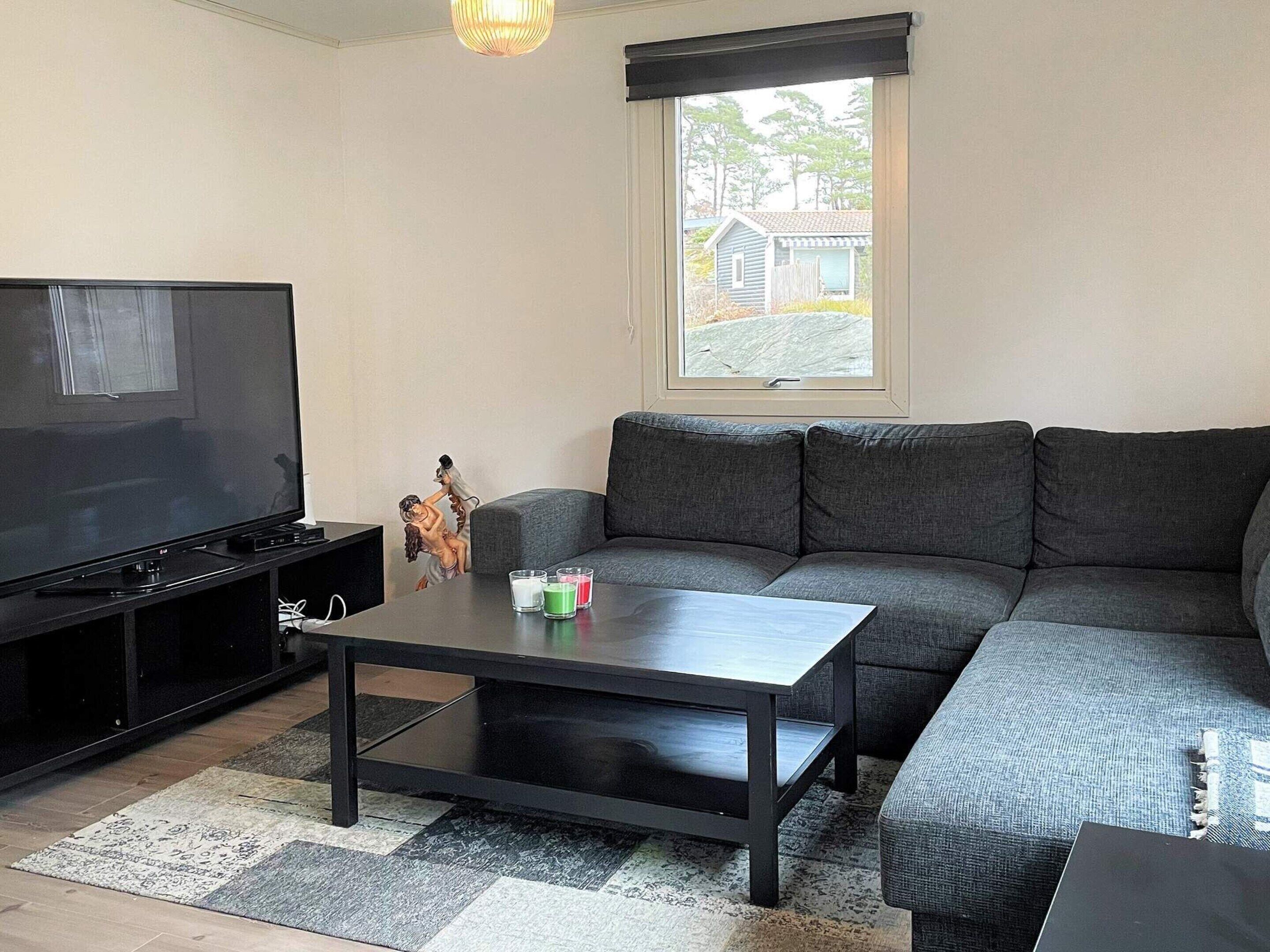 En stue med et fladskærms-tv, en grå sofa, et sofabord og en lille statue.