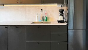 Cocina moderna con refrigerador de acero inoxidable, cafetera y lavamanos con artículos de aseo.