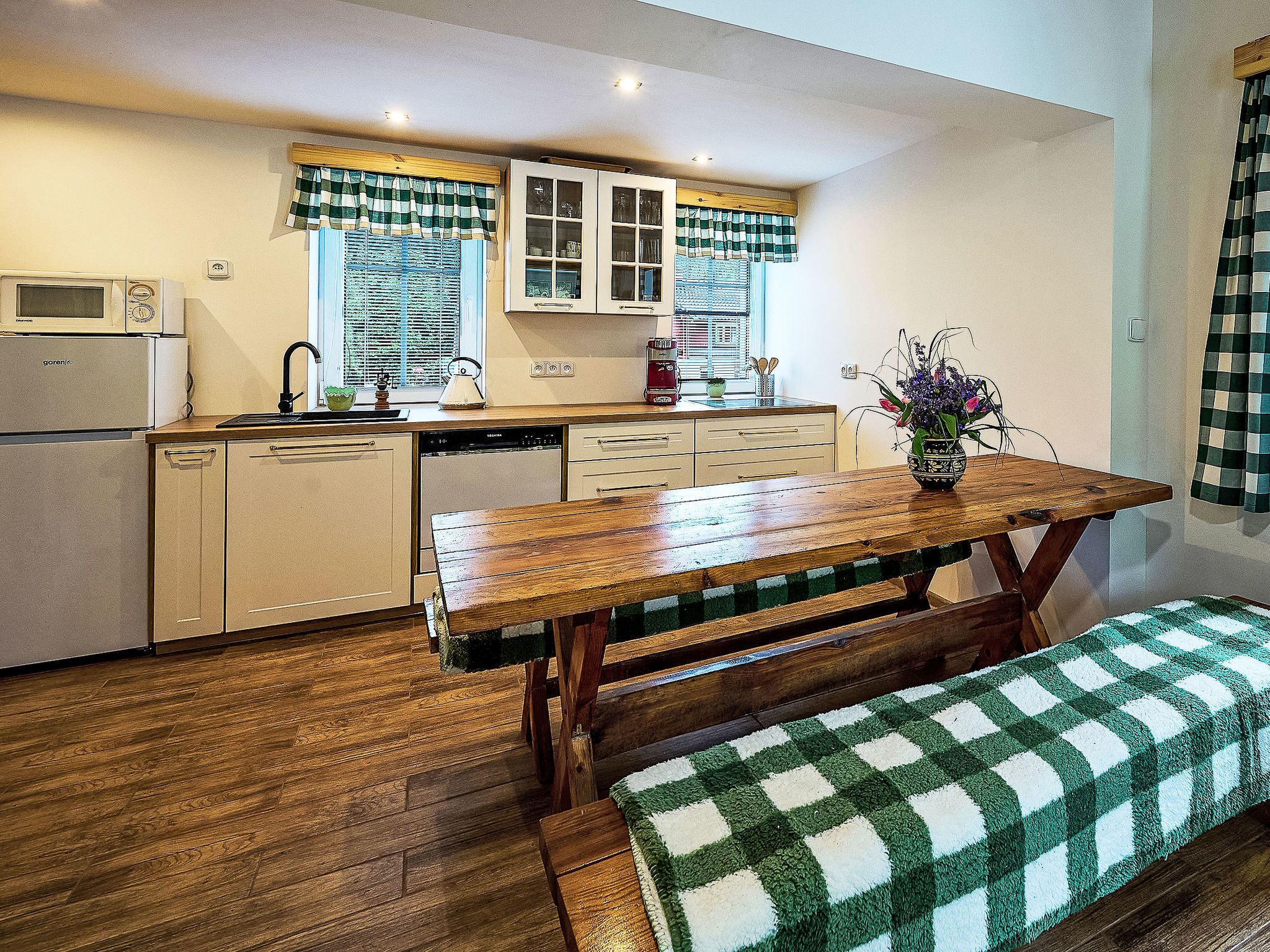 Una cocina compacta con una mesa de madera, una banca y un tapete a cuadros.