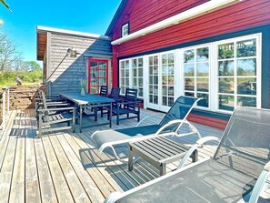 A wooden deck with a table and chairs, a red door, and large windows. - 5 Star Holiday Home in Borgholm (Borgholm)
