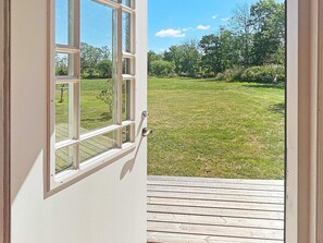 A view through a window of a grassy yard with a wooden deck. - 5 Star Holiday Home in Borgholm (Borgholm)