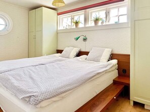 A bedroom with a bed, a wardrobe, a window with plants, and a wall-mounted lamp. - 5 Star Holiday Home in Borgholm (Borgholm)
