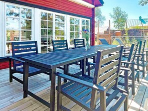 An outdoor deck with a wooden table and chairs, a red building with large windows, and a clear sky. - 5 Star Holiday Home in Borgholm (Borgholm)