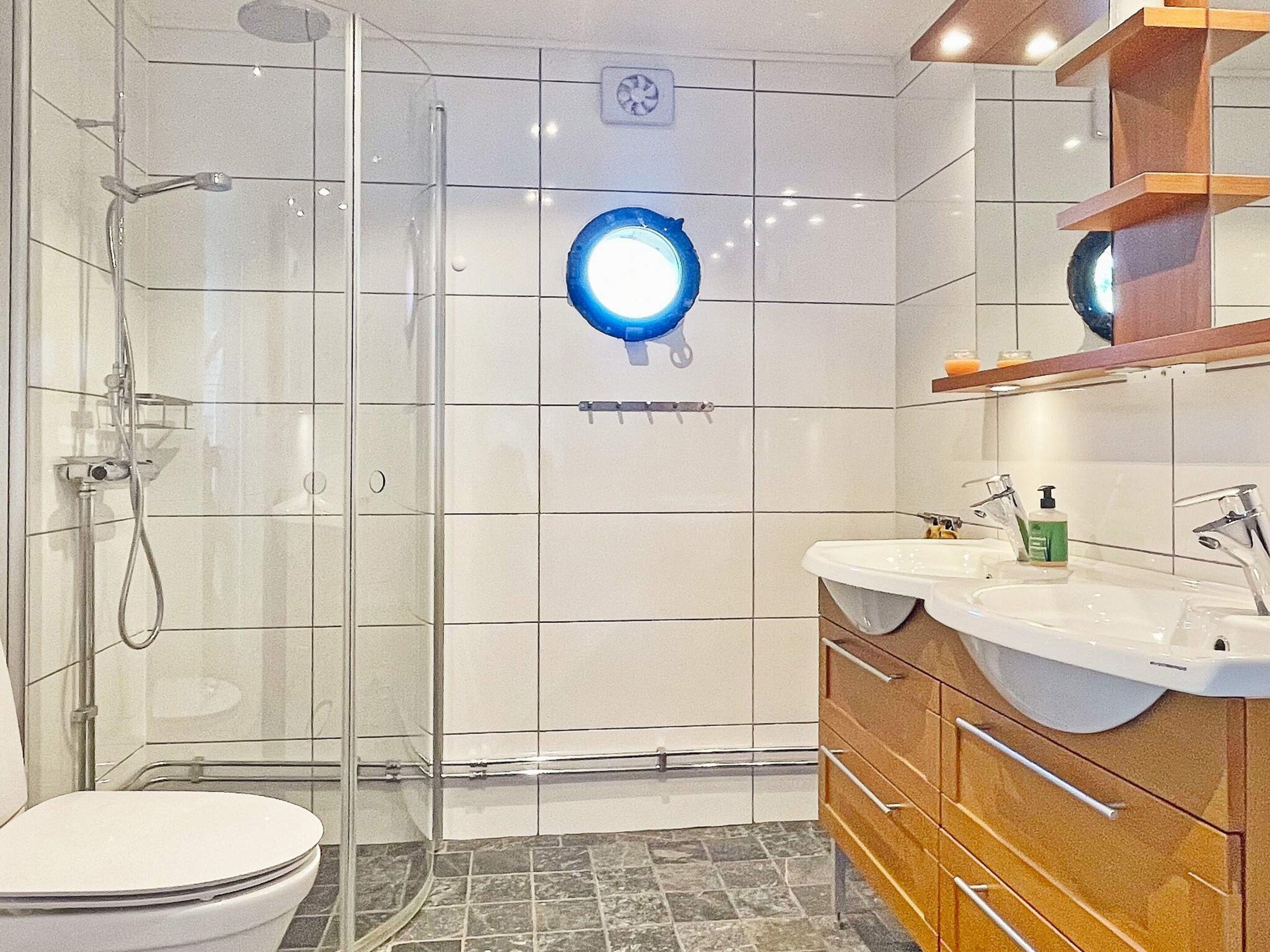 Een moderne badkamer met een douchecabine van glas, een wit toilet en een wastafel met spiegel en wasbak.