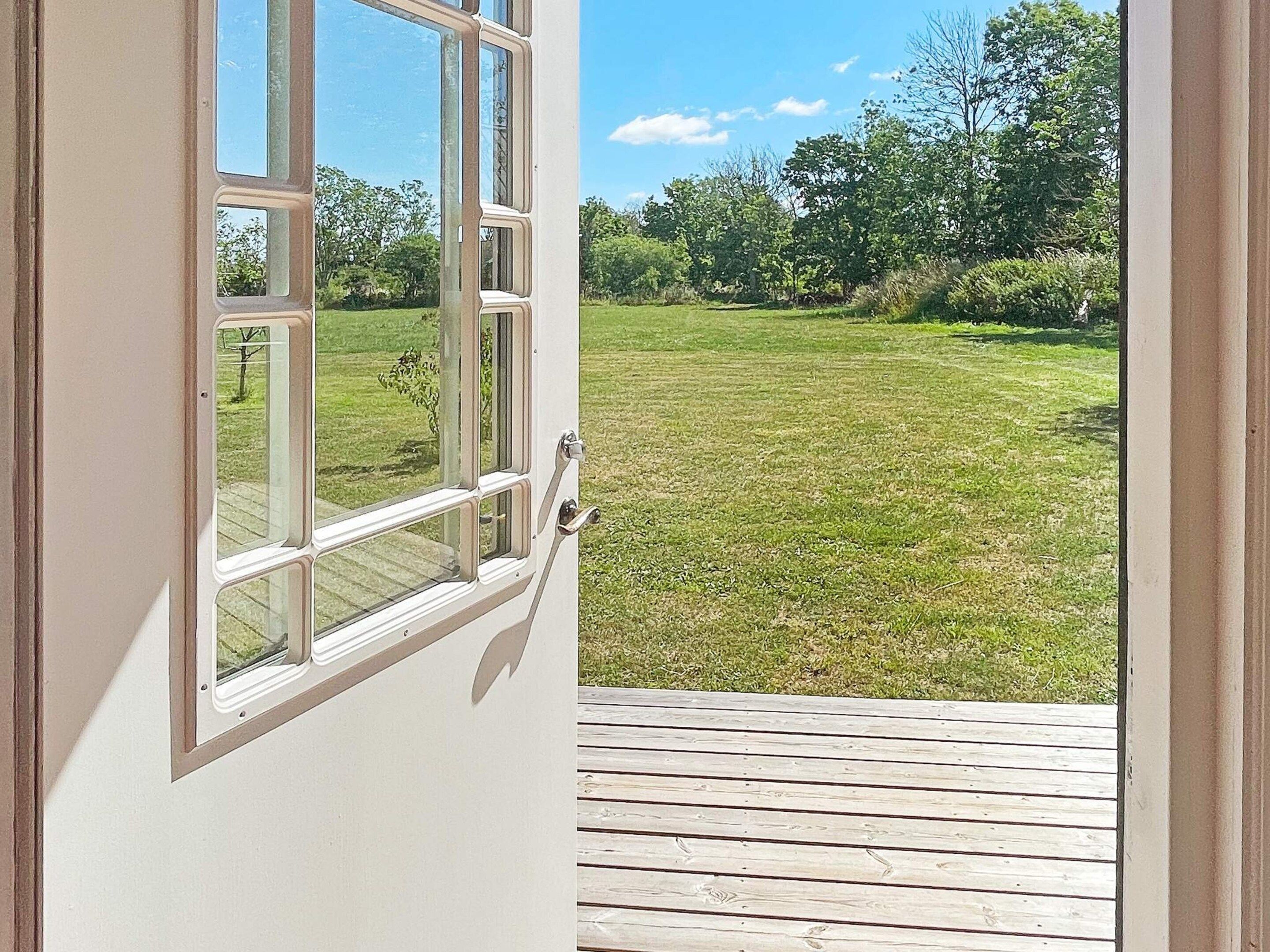 A view through a window of a grassy yard with a wooden deck.
