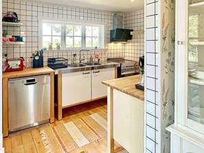 A kitchen with white cabinets, a dishwasher, a stove, and a window. - 5 Star Holiday Home in Borgholm (Borgholm)