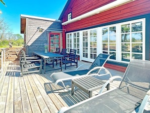 A wooden deck with a table and chairs, a red door, and large windows. - 5 Star Holiday Home in Borgholm (Borgholm)