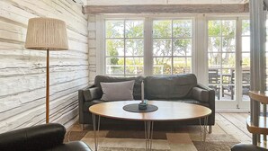 A cozy living room with a sofa, two armchairs, a coffee table, and a lamp. Large windows provide a view of the outdoors. - 5 Star Holiday Home in Borgholm (Borgholm)