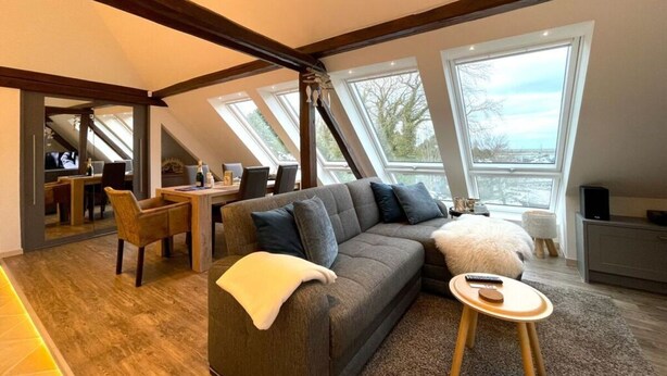 A loft-style room with a sofa, a small round table, and a dining area with a view through large windows.