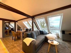 Un espace de vie de style loft comprenant un canapé, une petite table ronde et un coin repas offrant une vue dégagée grâce à de grandes fenêtres.
