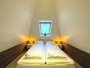 A twin bed in a room with a sloped ceiling and a skylight.
