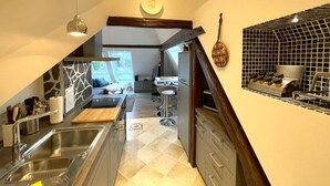A modern kitchen with a central island, a dining area with a high ceiling, and a view of the outdoors.