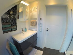 A modern bathroom with a white sink, a mirror, a towel rack, and a door.