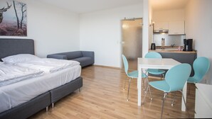 A modern room with a bed, a sofa, a dining table with chairs, and a kitchen area. - Apartment mit Balkon in Waldnhhe (Winterberg)