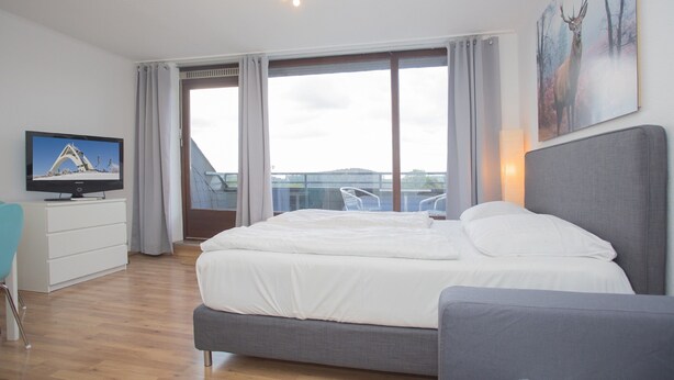 A modern hotel room with a large bed, a flat-screen TV, a balcony with a view, and a painting on the wall. - Apartment mit Balkon in Waldnhhe (Winterberg)