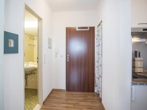 A hallway with a wooden door, a bathroom visible to the left, and a kitchen area to the right.