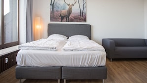 A modern bedroom with a large bed, a grey sofa, and a deer painting on the wall. - Apartment mit Balkon in Waldnhhe (Winterberg)