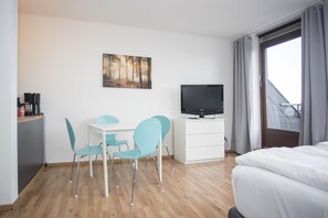 Une chambre d’hôtel moderne, équipée d’un lit, d’un bureau avec un téléviseur à écran plat, de deux chaises et d’un tableau au mur.
