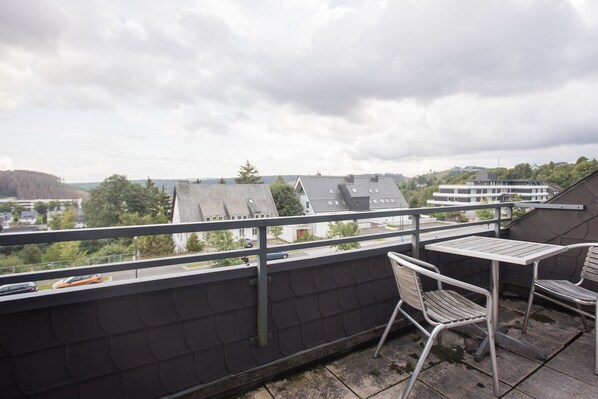 Un balcon avec une table et des chaises, donnant sur un quartier résidentiel avec des maisons et des arbres.