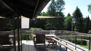 A wooden deck with outdoor furniture, a metal railing, and a view of trees. - Holiday Home Huus Adele (Holzminden)