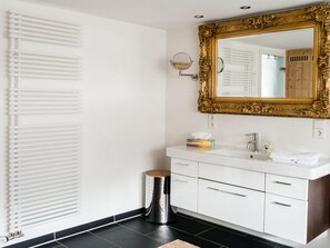 A modern bathroom with a white vanity, a gold-framed mirror, and a radiator.
