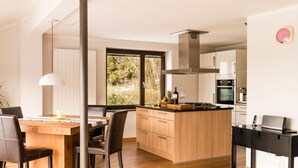 A modern kitchen with wooden cabinets, a central island, and a dining area with a table and chairs. - Holiday Home Huus Adele (Holzminden)