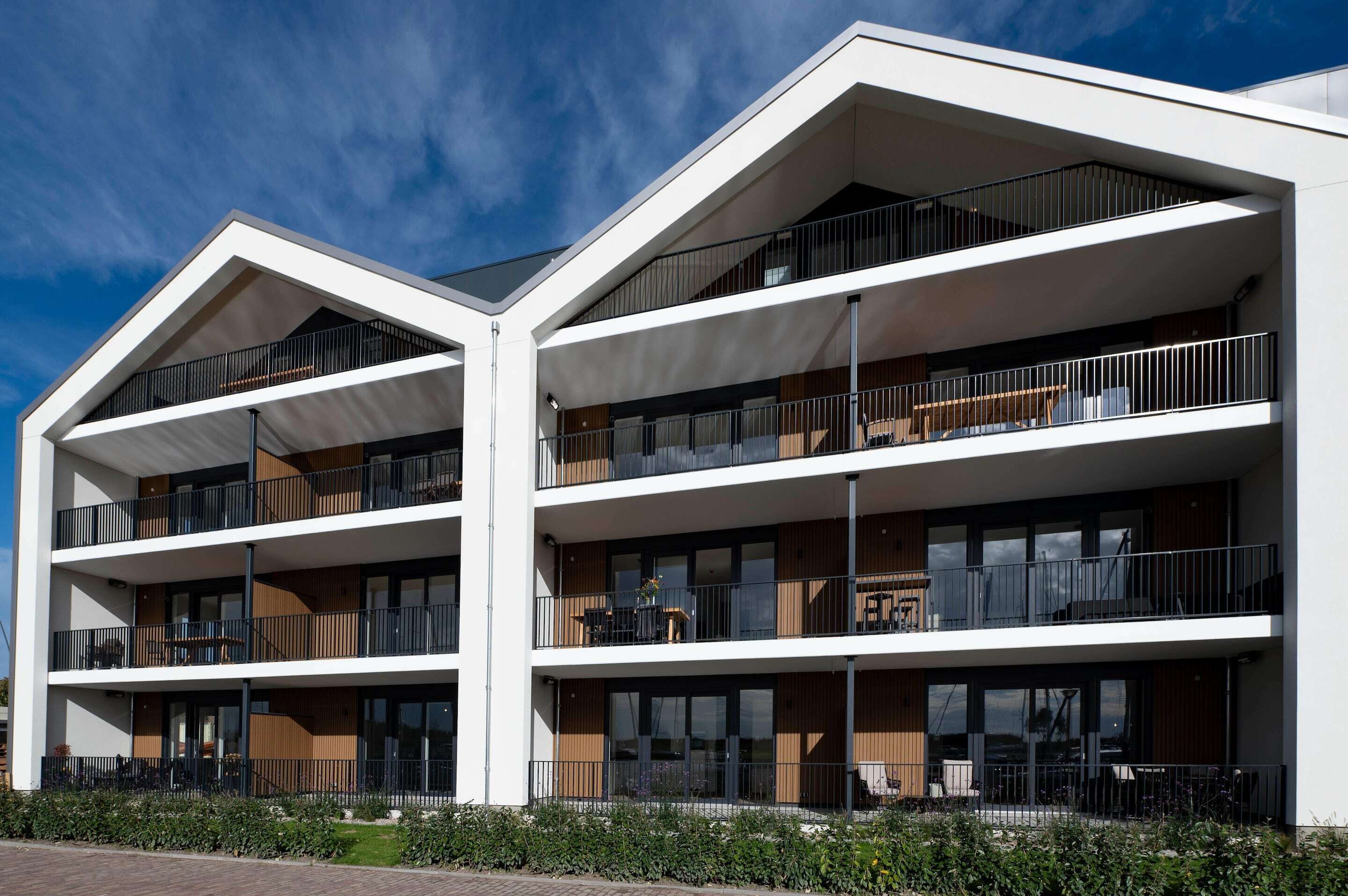 A modern multi-story building with balconies, large windows, and a flat roof.