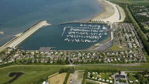 An aerial view of a coastal marina with boats docked, surrounded by residential housing and a sandy beach. - Stylish Marina Loft W/balcony (Kamperland)