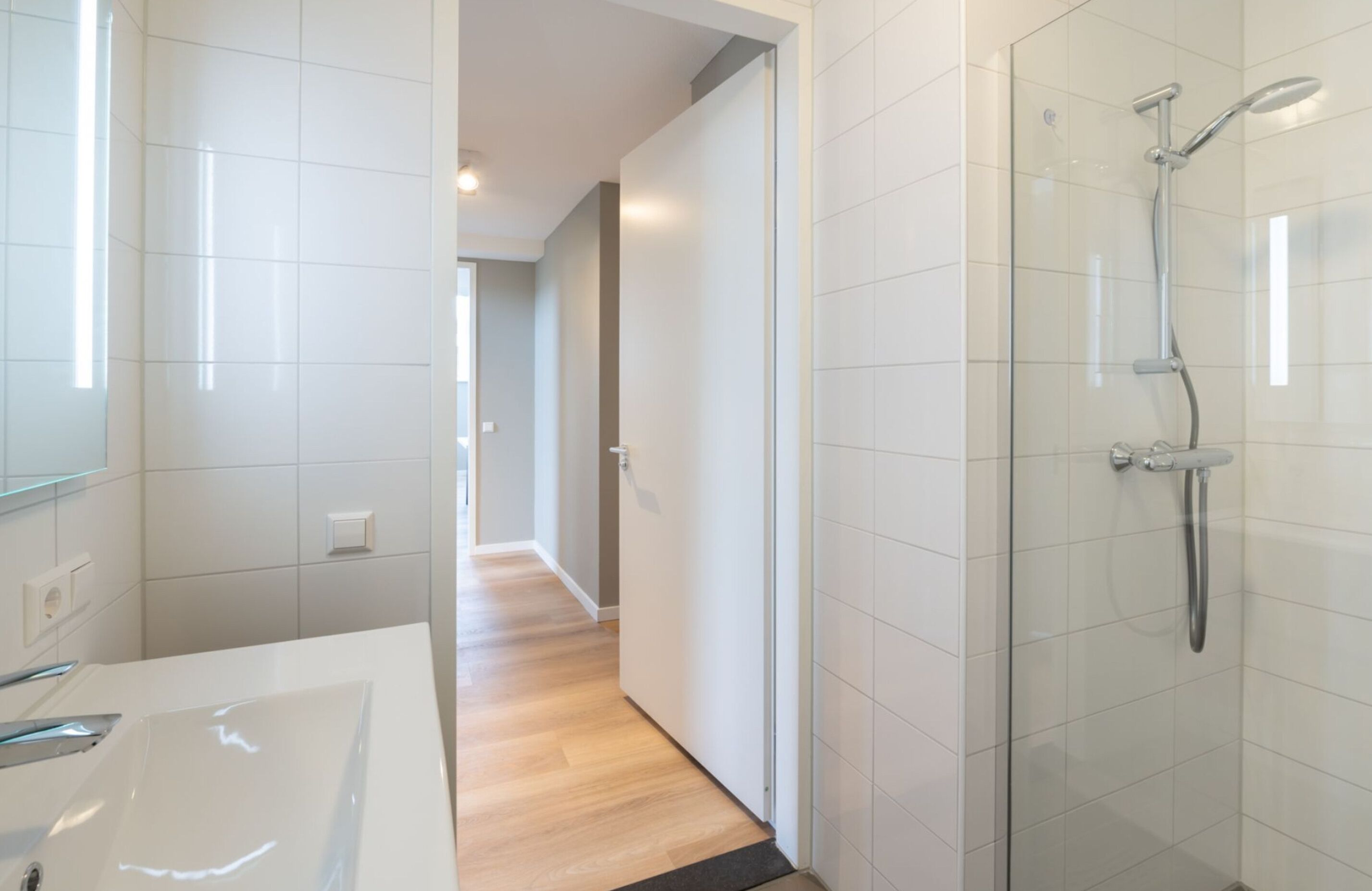 A modern bathroom with a glass shower enclosure, a white sink, and a wooden floor.