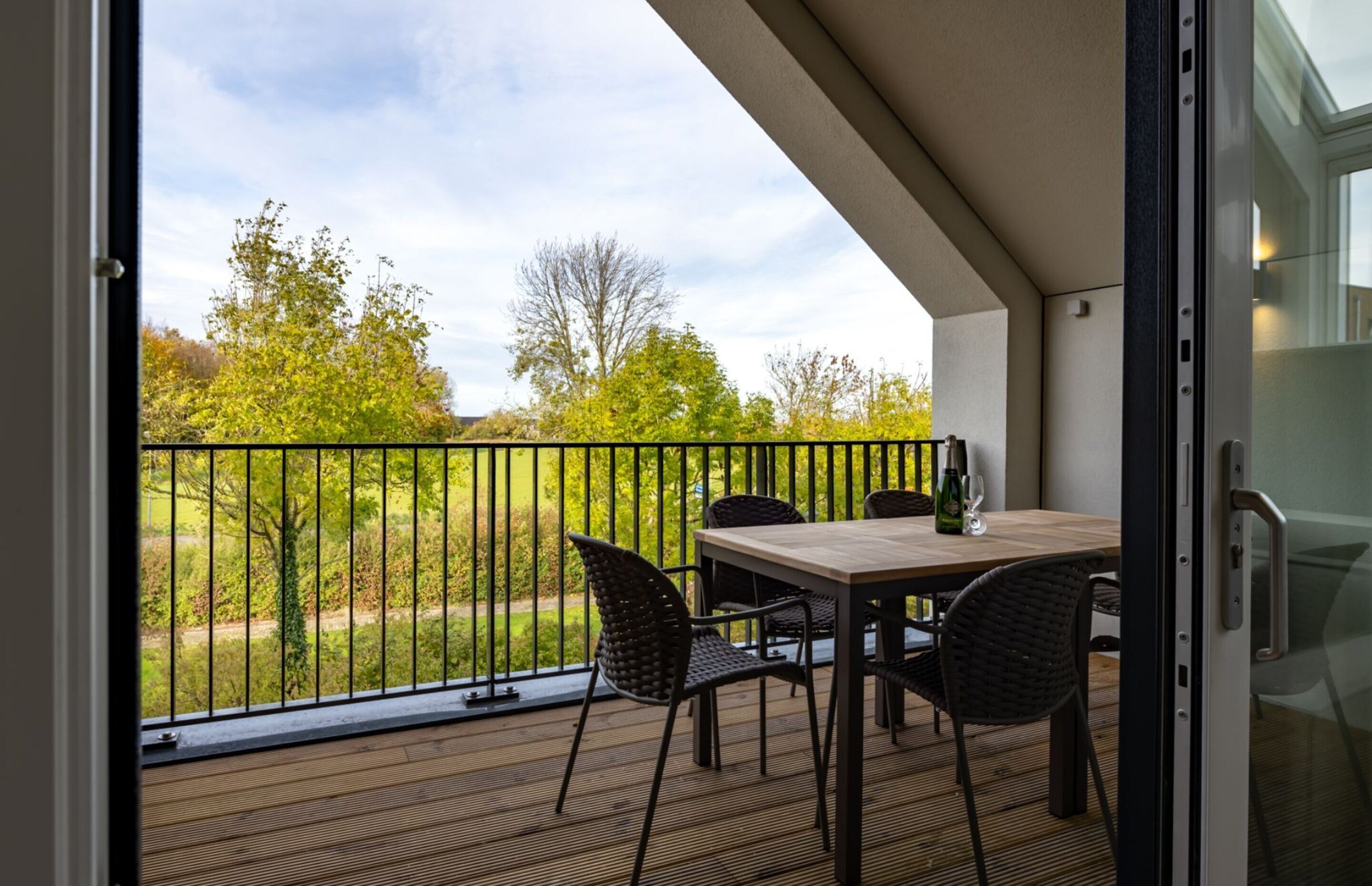 A balcony with a table and chairs, a glass door, and a view of a green landscape.