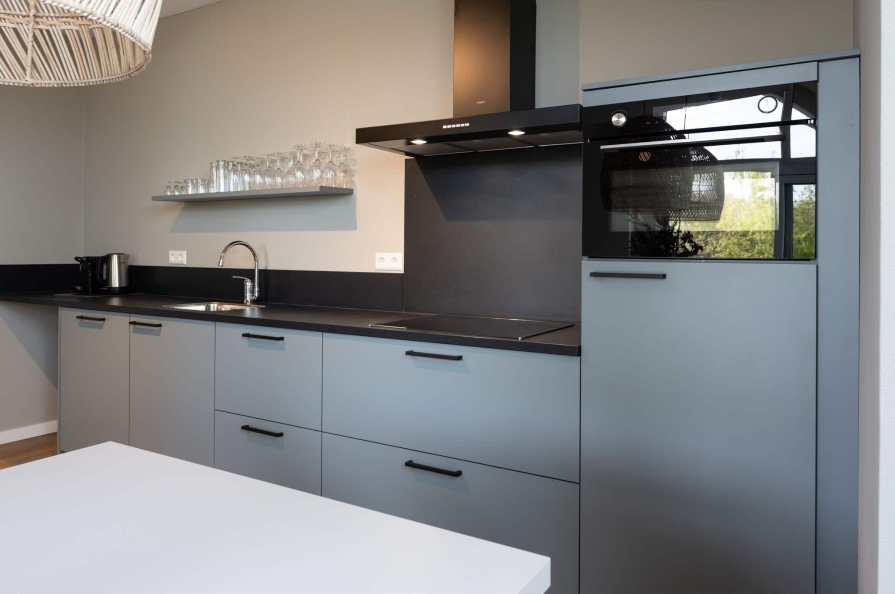 Eine moderne Küche mit grauen Schränken, einer schwarzen Arbeitsplatte, einer Edelstahl-Spüle und einem eingebauten Backofen.