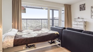 A bedroom with a bed, a sofa, a window with curtains, and a white cabinet. - Spacious Studio With Storage Room (Blankenberge)