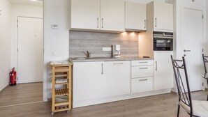 A modern kitchen with white cabinets, a built-in oven, and a coffee maker. - Spacious Studio With Storage Room (Blankenberge)